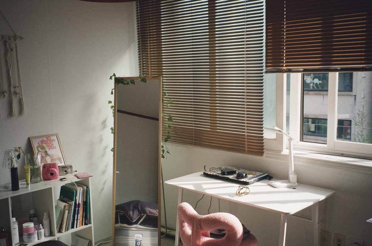 Bright room with a desk, pink chair, and window blinds.